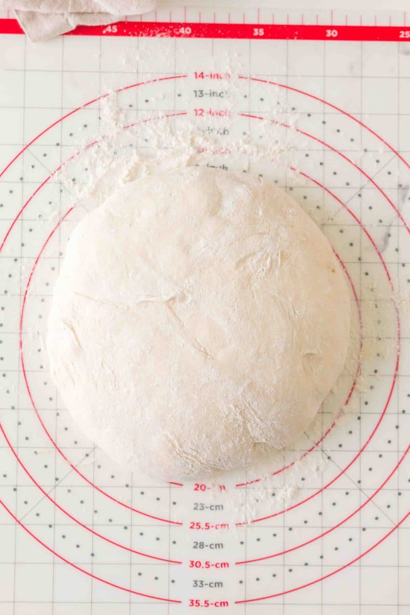 A soft and puffy risen ball of dough sitting on a flour dusted pastry mat ready for shaping. Hostess At Heart