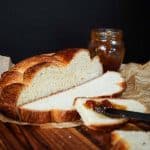A loaf of Hungarian Egg Twist Bread with the front slices cut from the front. A jar of jam sits in the background and a knife with jam sits on the front slice of bread. Hostess At Heart