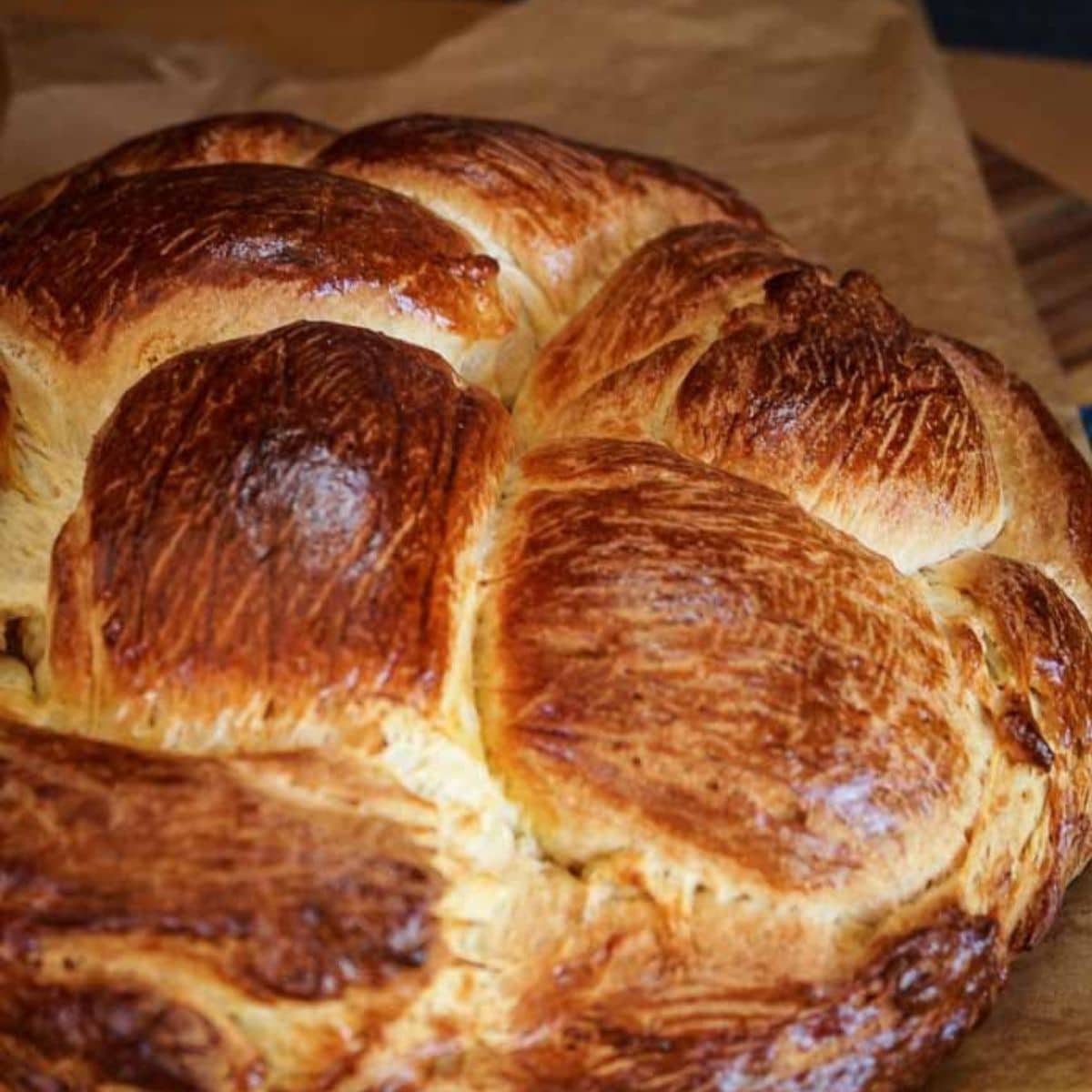 A close up of a loaf of a golden brown round loaf of Hungarian Egg Twist Bread sitting on a piece of parchment paper. Hostess At Heart