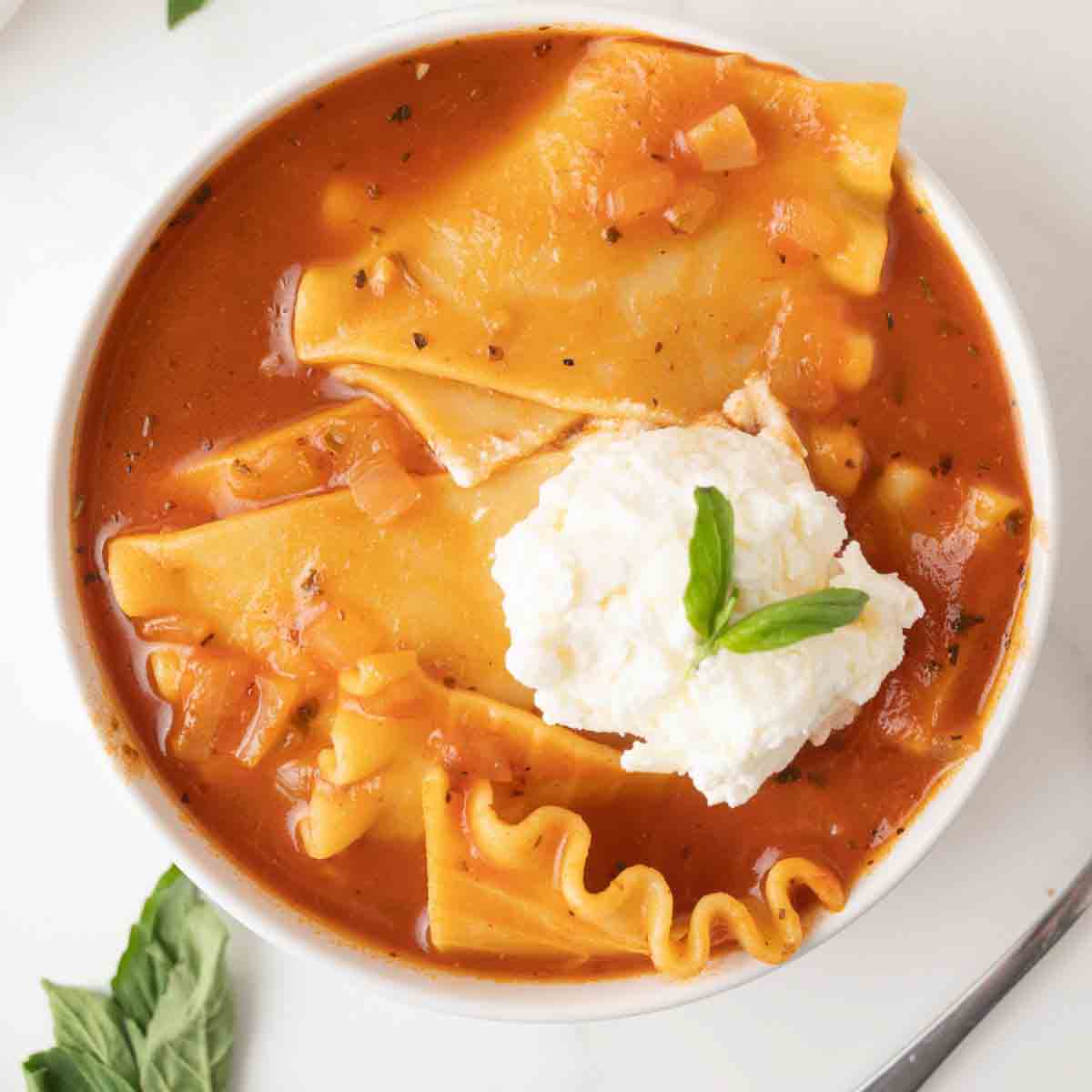 Top down view of lasagna soup with broken noodles in a rich tomato broth topped with cheese and fresh basil. Hostess At Heart