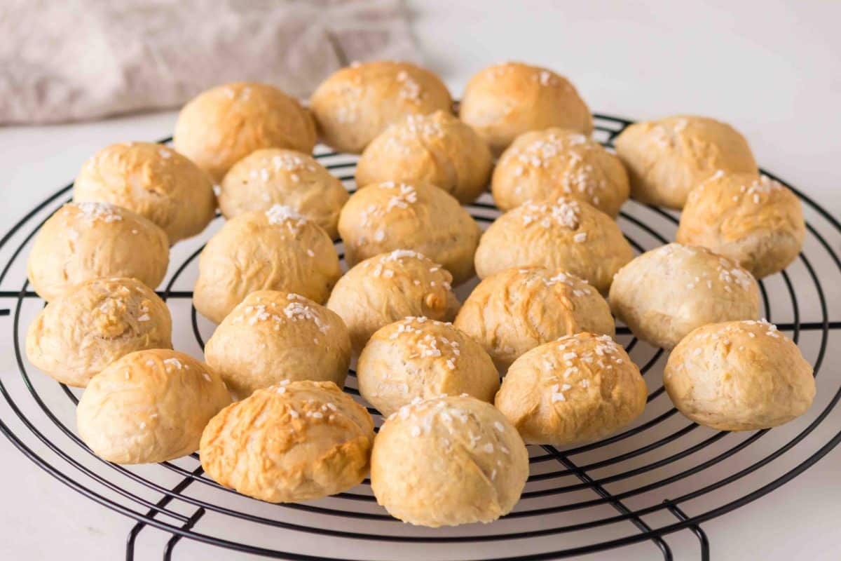 Sideview of baked golden brown soft pretzel rolls from scratch on a cooling rack. Hostess At Heart