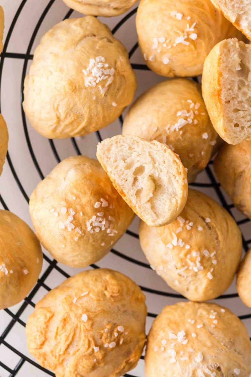 Golden homemade pretzel rolls sprinkled with coarse sea salt on a cooling rack. Hostess At Heart
