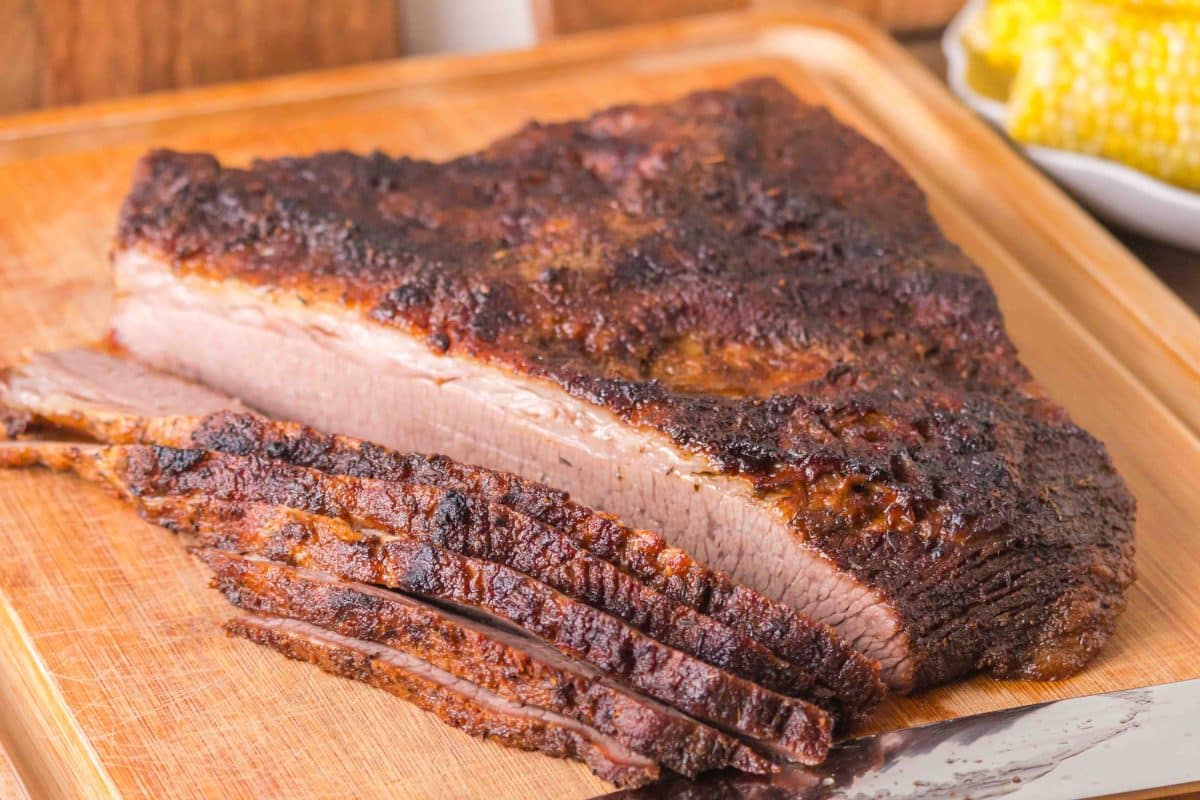 A tableview of an oven baked brisket with a juicy brown bark sitting on a cutting board with 5 slices fanned out in front of it ready for serving. Hostess At Heart