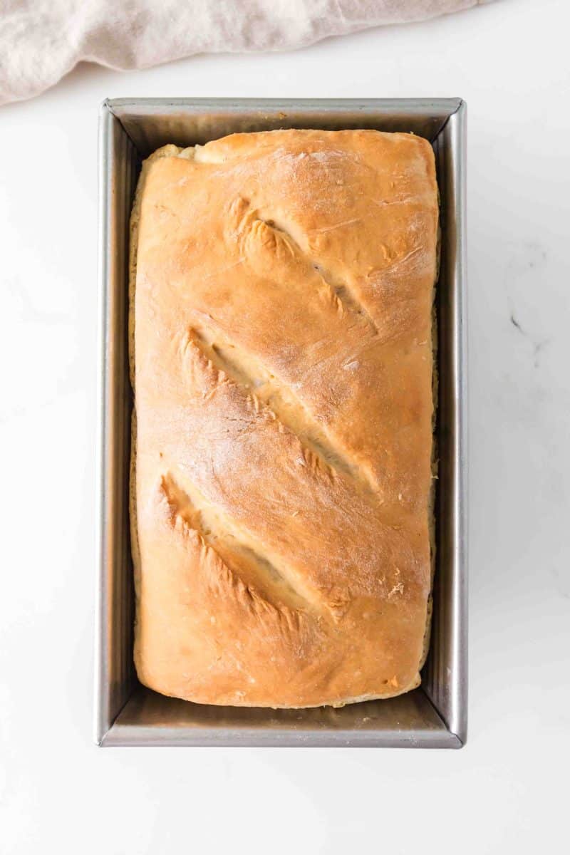 A golden-brown homemade bread loaf baked from no knead dough in a 9x5 loaf pan. Hostess At Heart