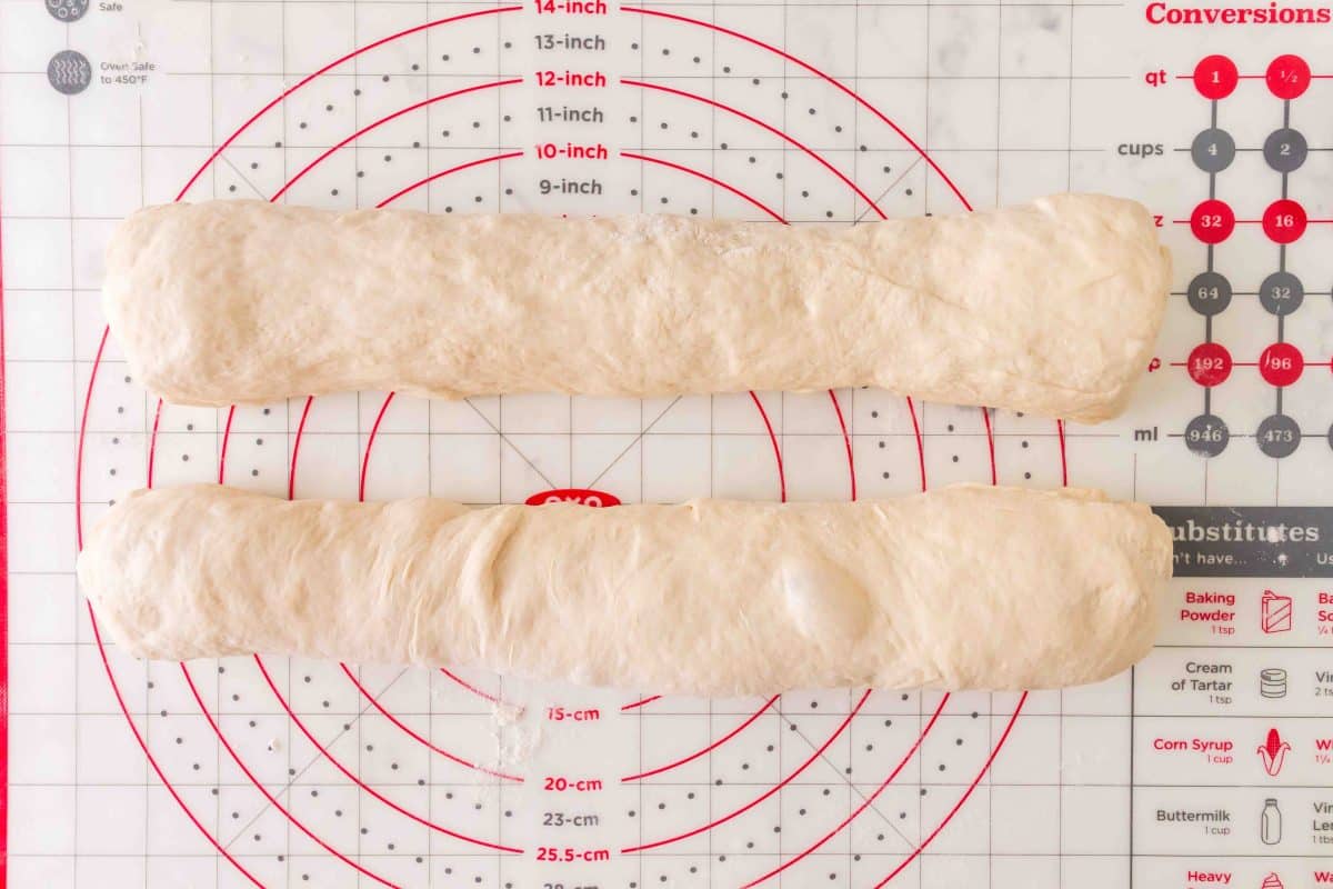 Two baguettes of French bread dough rolled into baguette log shapes on a pastry mat. Hostess At Heart