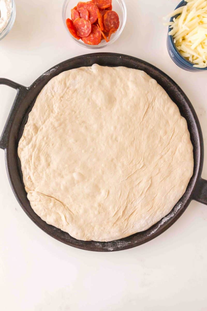 No knead pizza dough spread into a cast iron skillet for pre-baking. Hostess At Heart