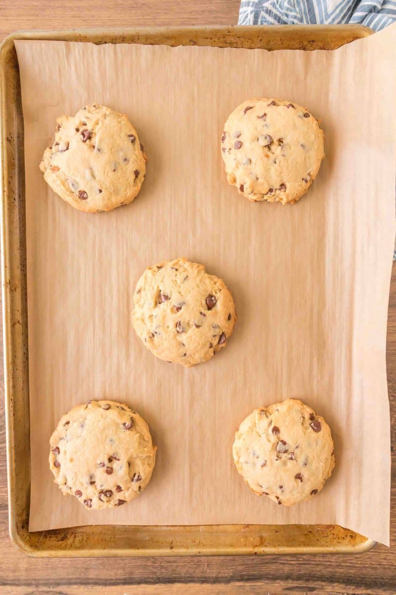 Freshly baked crumbl cookies chocolate chip on a parchment-lined baking sheet. Hostess At Heart