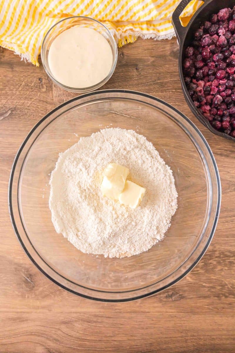 Butter added to a mixing bowl filled with a blend of flour, salt, baking powder, and baking soda to make a sourdough discard blueberry cobbler crust. Hostess At Heart