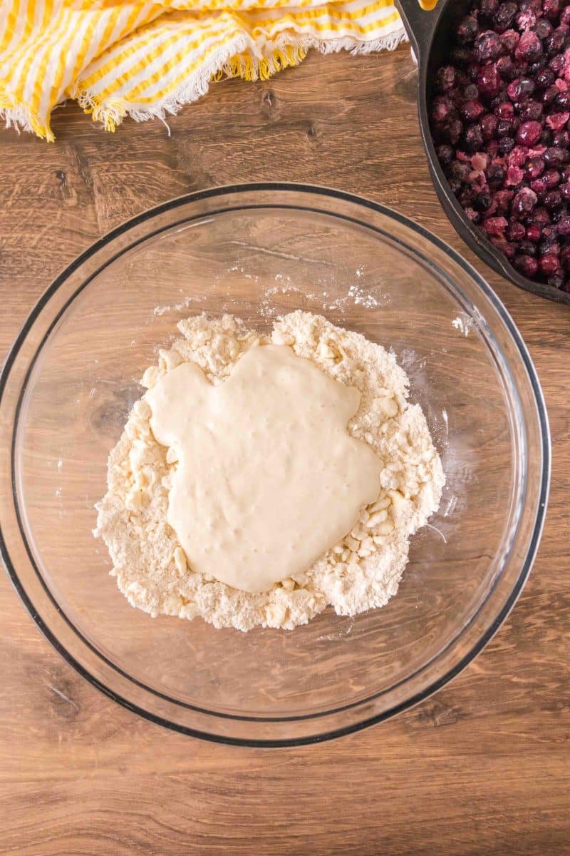 A large mixing bowl filled with blueberry cobbler crust ingredients: flour, baking powder, baking soda, salt, sugar and sourdough discard. Hostess At Heart