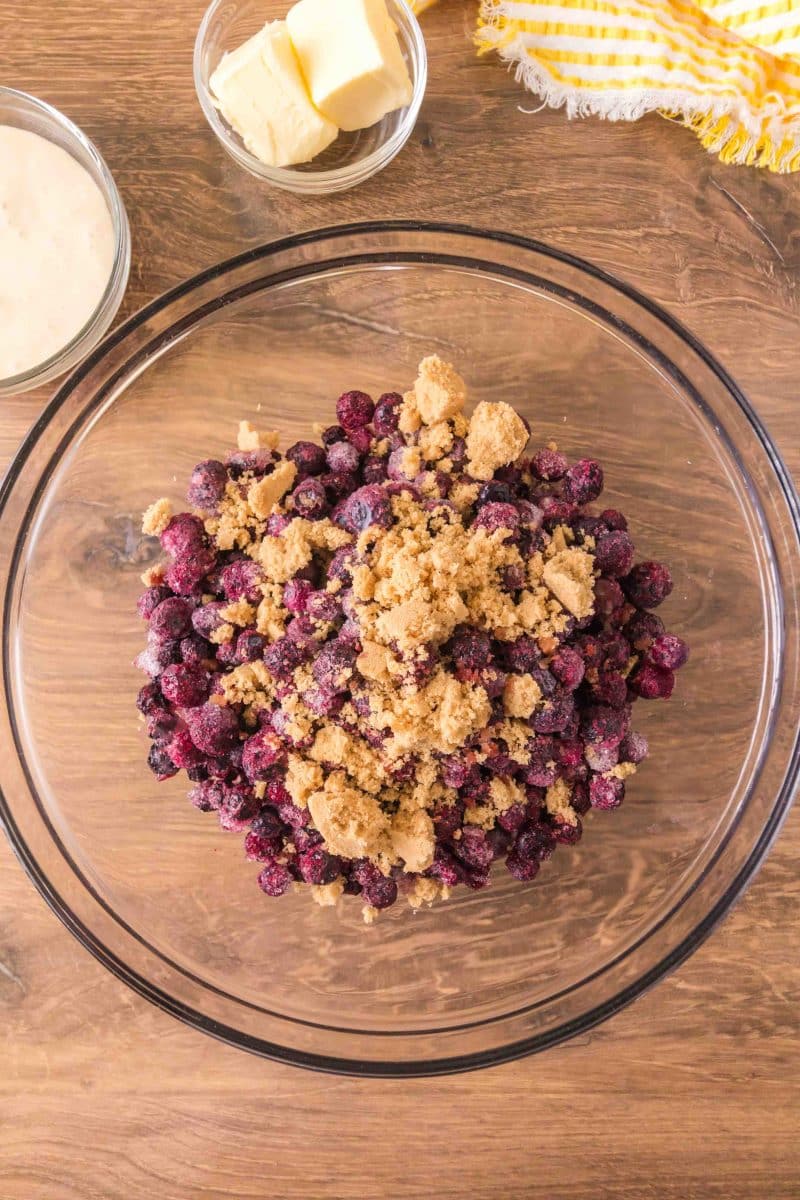 Frozen blueberries tossed with brown sugar, flour, and lemon juice in a large mixing bowl for sourdough blueberry cobbler filling. Hostess At Heart