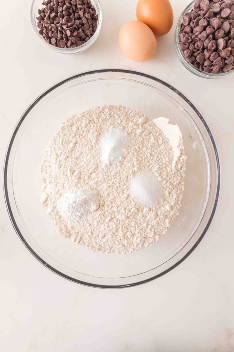 A mixing bowl filled with dry ingredients to make chocolate chip crumble cookies, flour, baking powder, baking soda, and salt. Hostess At Heart