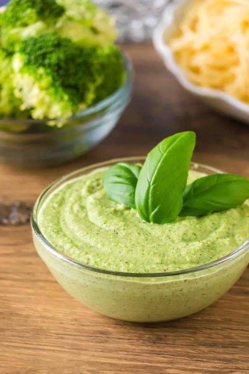 A finished broccoli pesto in a glass bowl garnished with fresh basil leaves. Hostess At Heart
