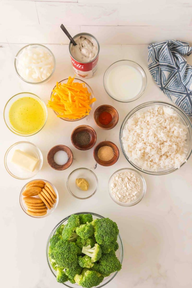Cheesy Broccoli rice casserole ingredients: fresh broccoli, flour, Ritz crackers, butter, onion, dijon mustard, paprika, cooked rice, chicken broth, garlic powder, salt and pepper, cream of mushroom soup, and milk. Hostess At Heart