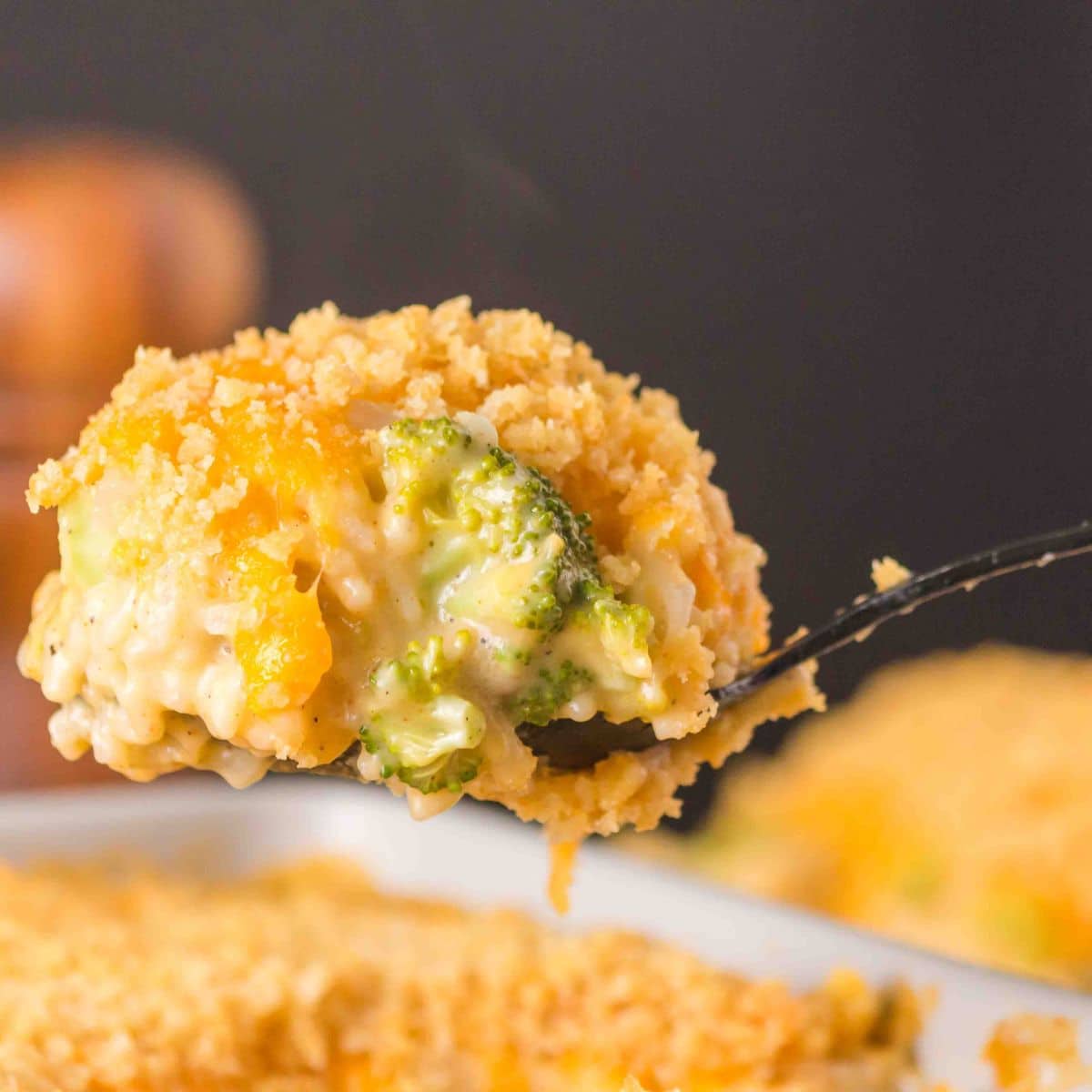 Close-up forkful of broccoli & rice casserole showing melted a melted creamy cheese in a sauce topped with crispy cracker topping. Hostess At Heart