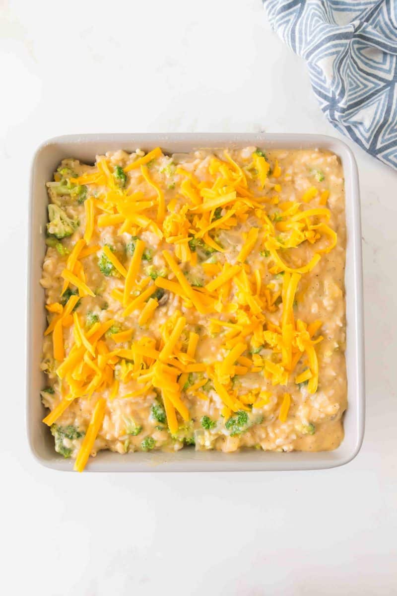 Unbaked broccoli rice casserole with cream of mushroom soup tossed with cheddar cheese and cracker crumbs in a 9x9 baking dish.