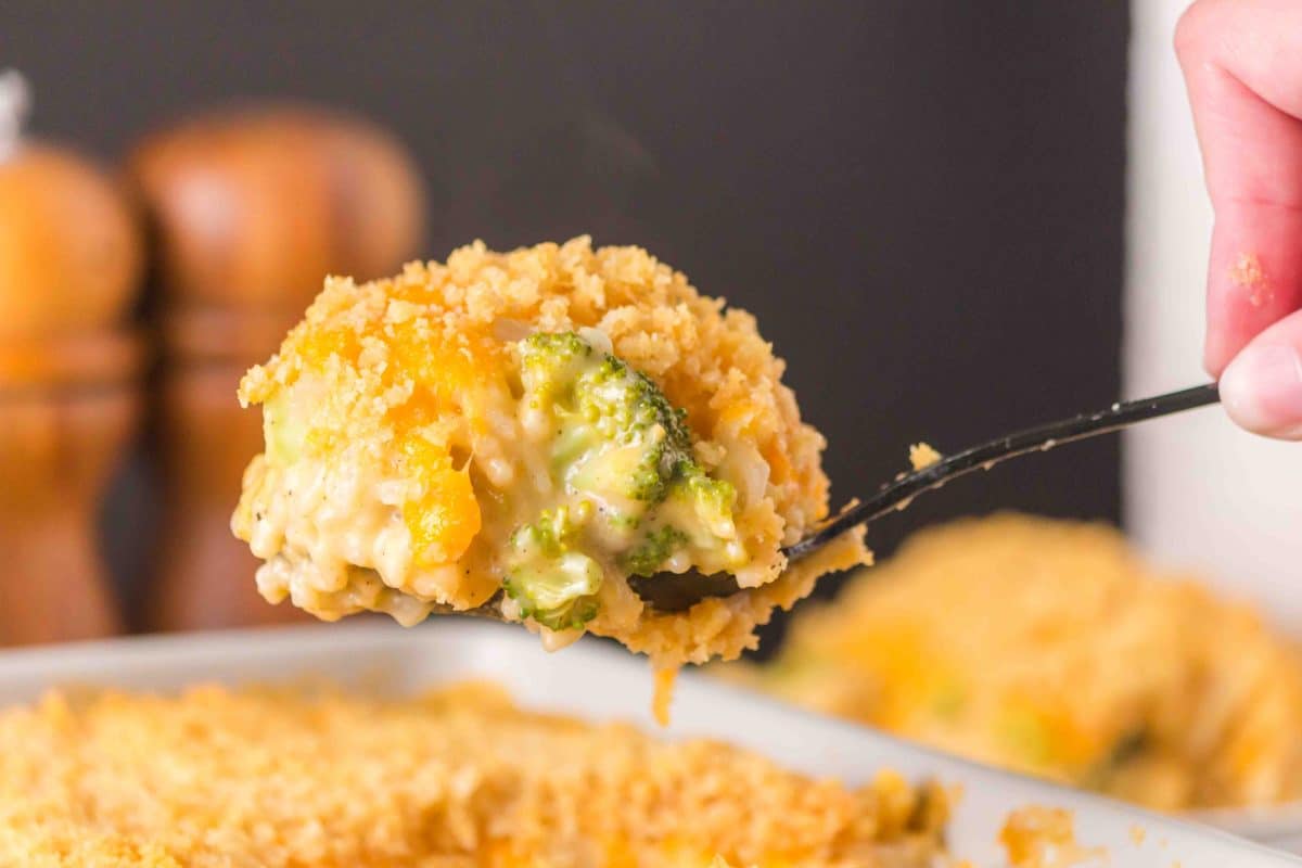 Close-up forkful of broccoli rice casserole showing melted cheese and crispy cracker topping. Hostess At Heart