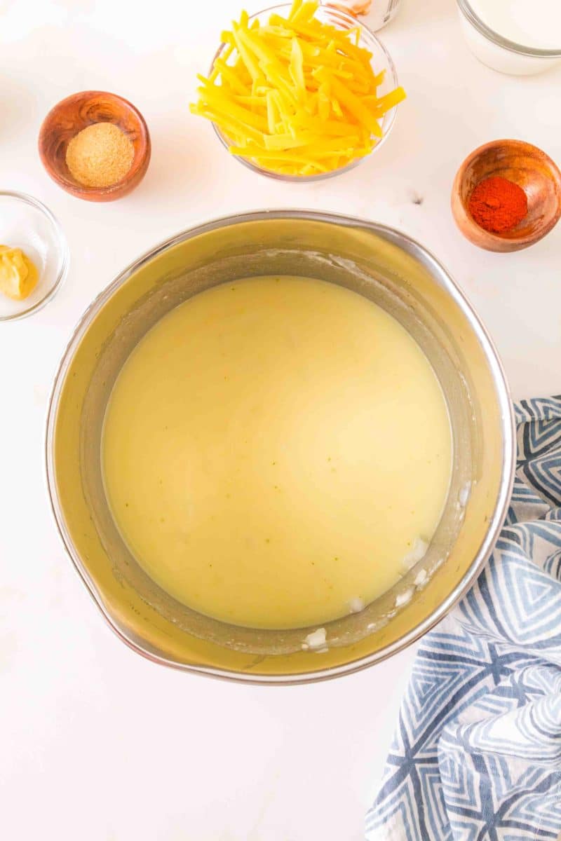 Top down view of a smooth cheese sauce thickening in a saucepan on the stove. Hostess At Heart