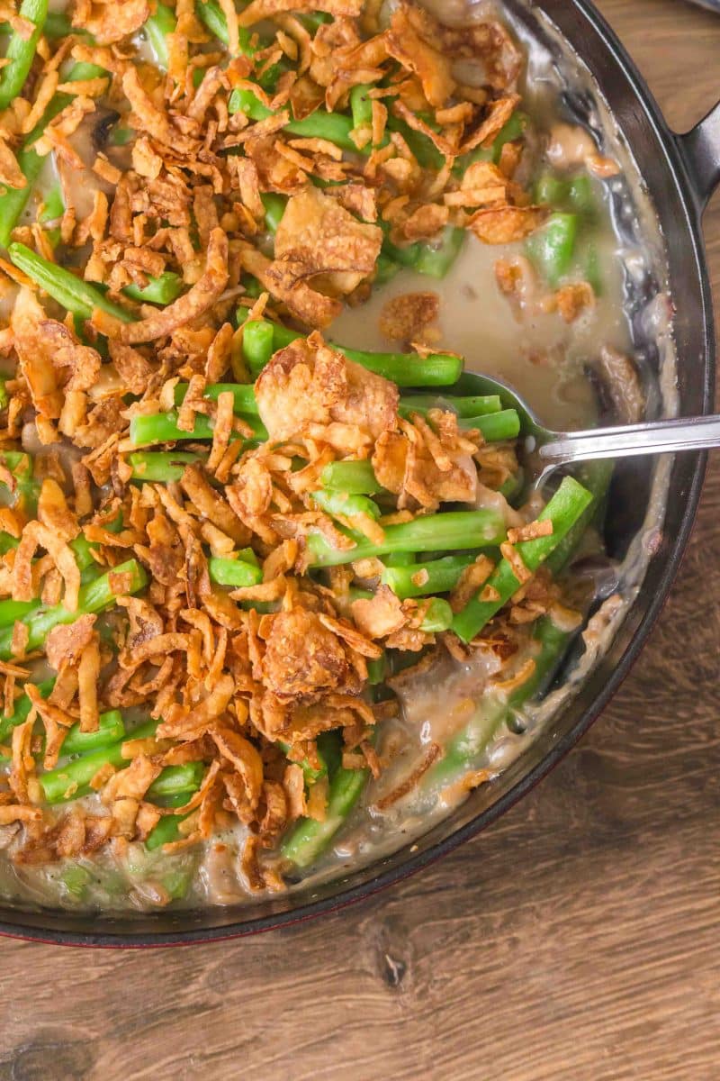 Spoon lifting a serving of green bean casserole with fresh green beans. Hostess At Heart