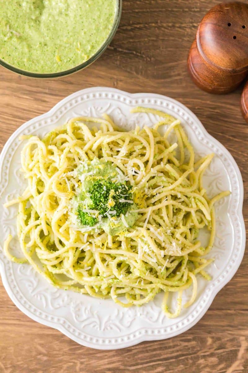 Overhead shot of broccoli pesto pasta tossed with spaghetti and topped with Parmesan and a garnish of a broccoli floret. Hostess At Heart