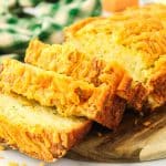 Sliced zucchini cheddar bread fanned out against the loaf on a wooden cutting board. Hostess At Heart.