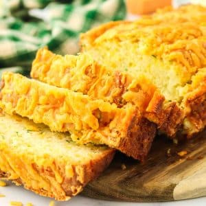 Sliced zucchini cheddar bread fanned out against the loaf on a wooden cutting board. Hostess At Heart.
