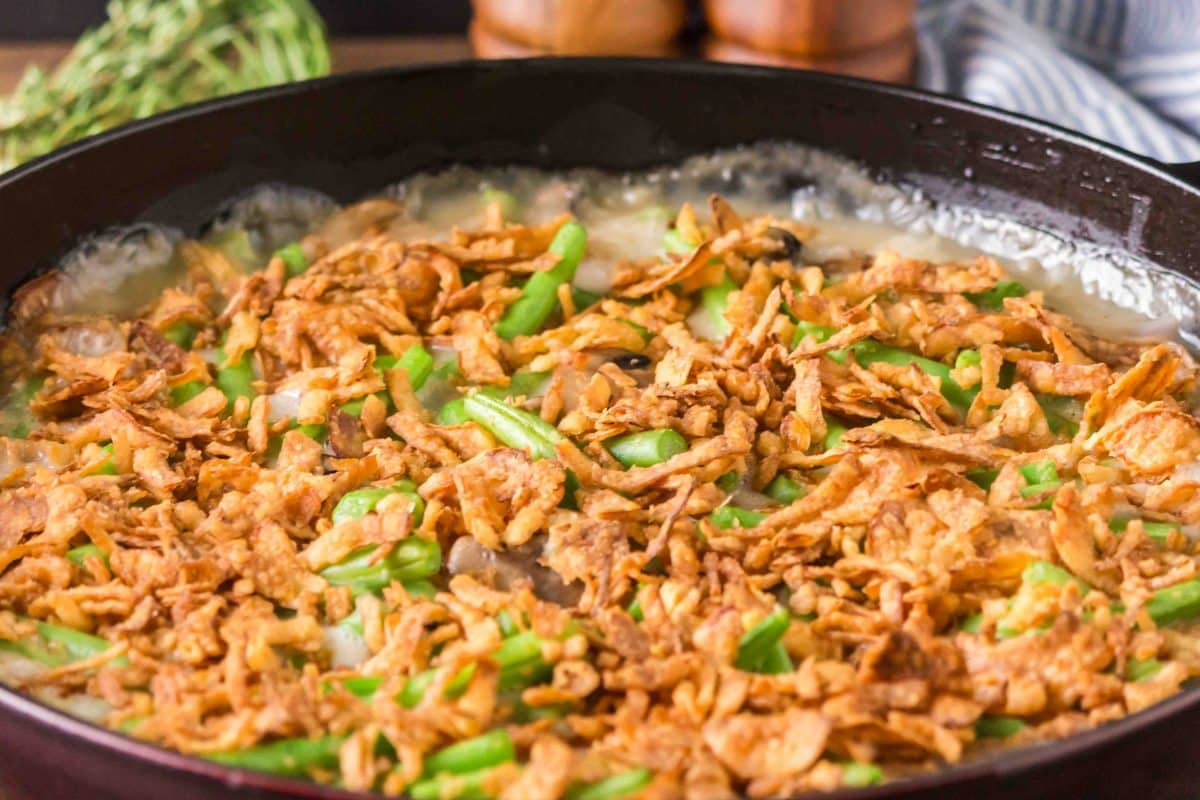 Tableview of a skillet of fresh green beans casserole topped with crispy fried onions in a thick mushroom sauce. Hostess At Heart