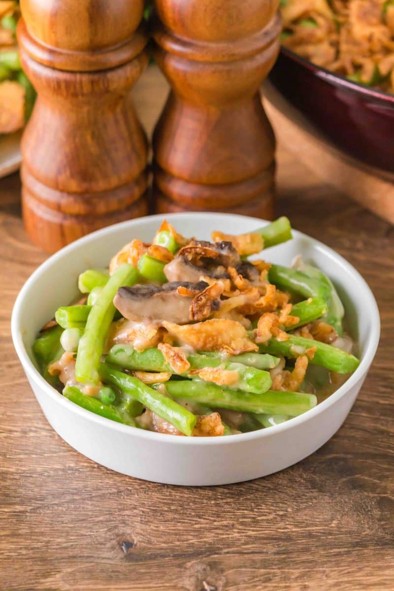 A white bowl filled with homemade green bean casserole topped with crispy cooked onions. Hostess At Heart