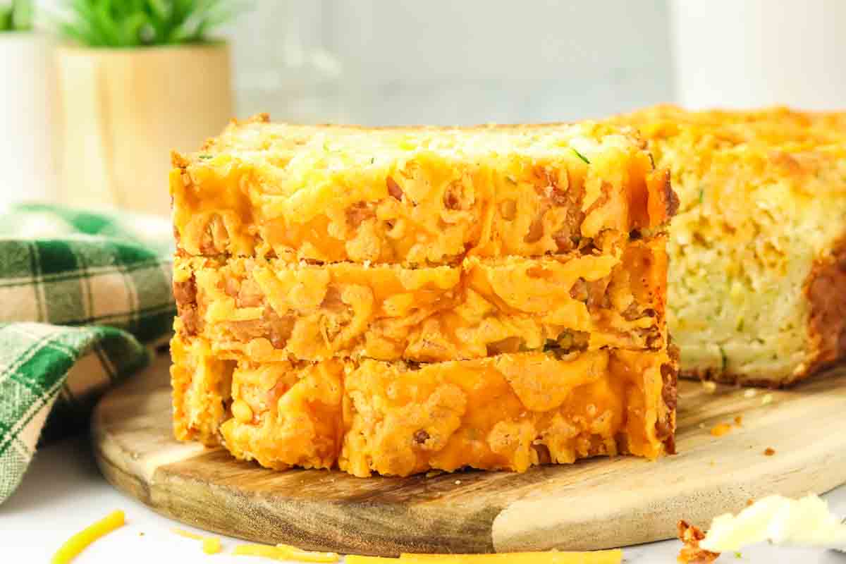 Tableview of three slices of zucchini cheddar bread stacked on top of each other showing a golden brown crispy cheese topping. Hostess At Heart