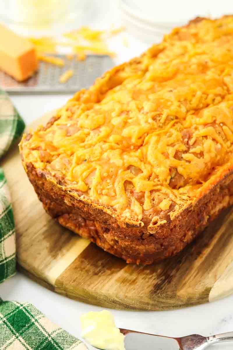 Angled view of a golden brown loaf of Zucchini Cheddar bread showing a crisp crunchy cheese topping. Hostess At Heart