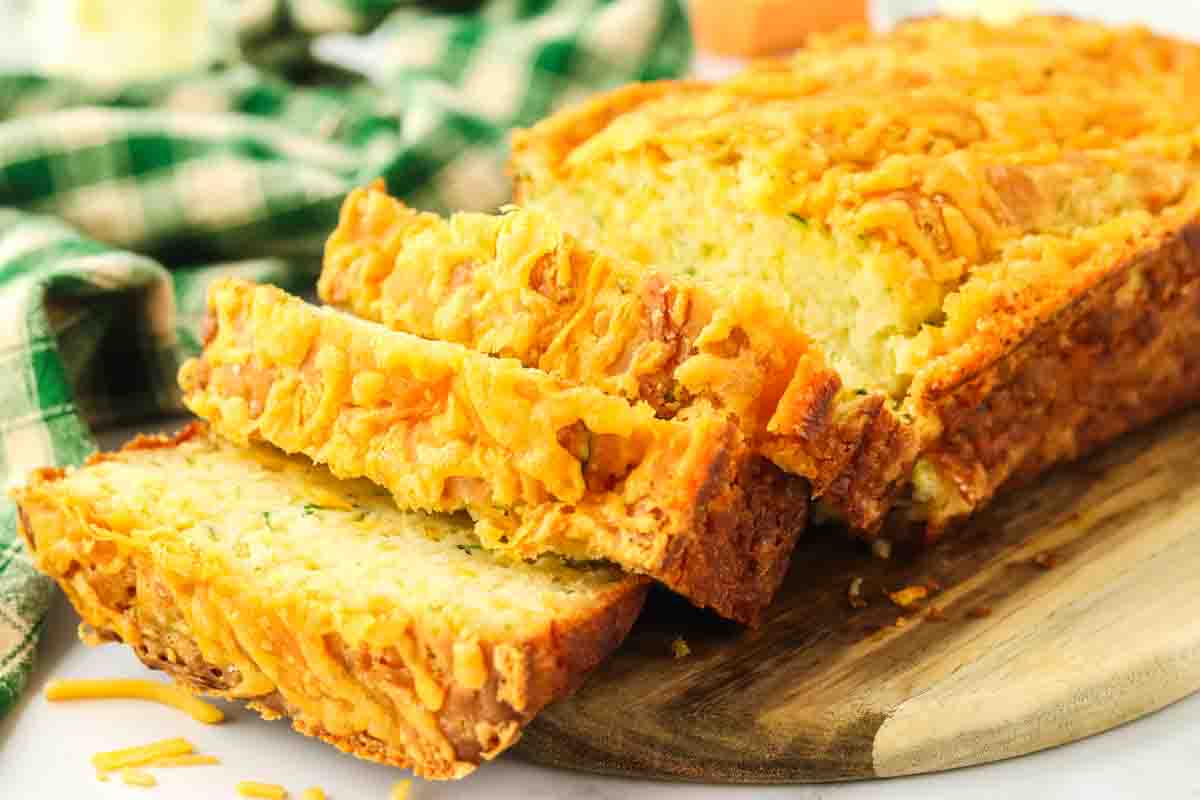 Sideview of sliced zucchini cheese bread fanned out in front of the loaf showing a moist cheesy interior. Hostess At Heart