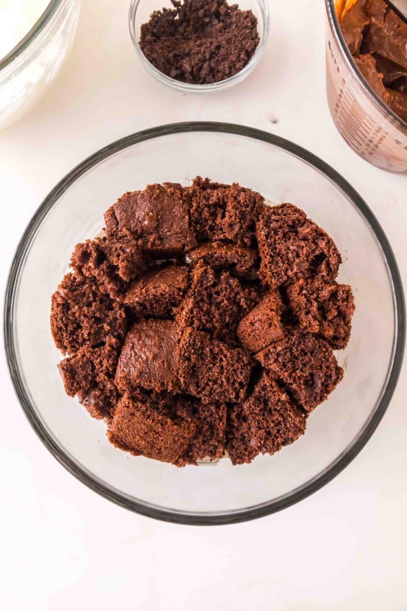 Chunks of chocolate cake in a glass mixing bowl ready to be made into a triffle dessert. Hostess At Heart
