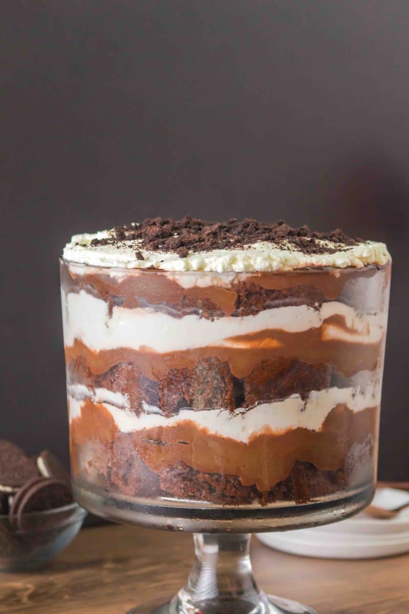 Side angle of a trifle bowl filled with layers of chocolate cake, pudding, whipped cream and oreo cookie crumbs. Hostess At Heart