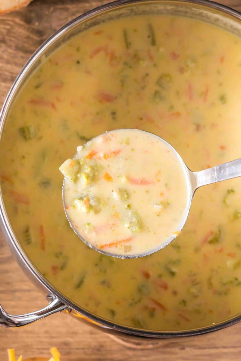 Top down view of a ladle filled with Creamy Broccoli Cheese Soup hovering over the soup pot. Hostess At Heart