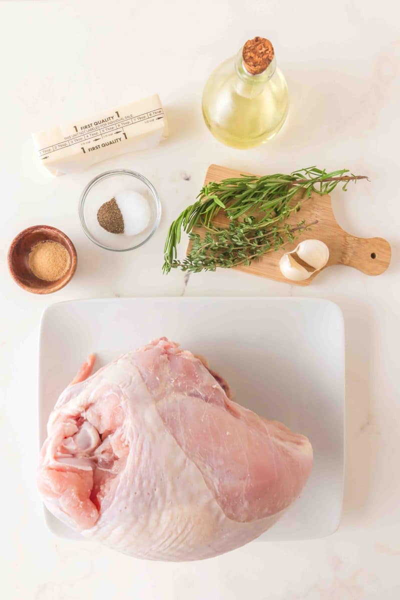 Ingredients used to make a roasted turkey breast recipe including a bone-in skin-on turkey breast, butter, olive oil, fresh rosemary and thyme, onion powder, salt and pepper, and garlic. Hostess At Heart
