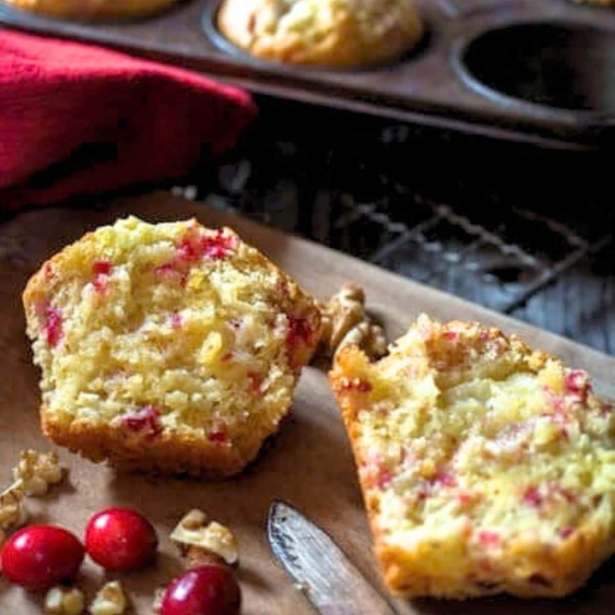 Top down view of a cranberry orange muffin split in half showing a soft crumb dotted with cranberries and chopped walnuts. Hostess At Heart