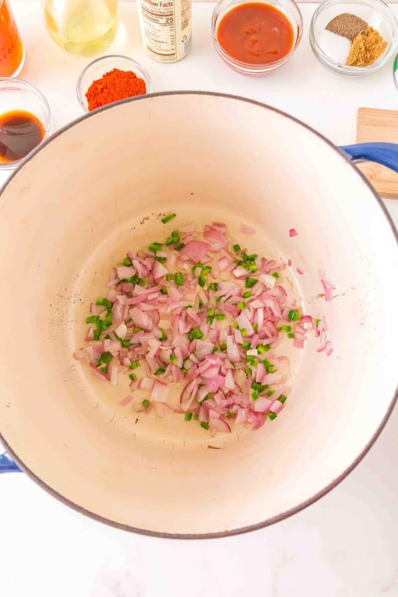 Top down view of a Dutch oven filled with diced and sauteed onion and jalapenos. Hostess At Heart