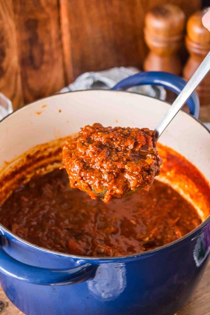 A ladle filled with thick beef chili made with leftover brisket hovering over a dutch oven. Hostess At Heart