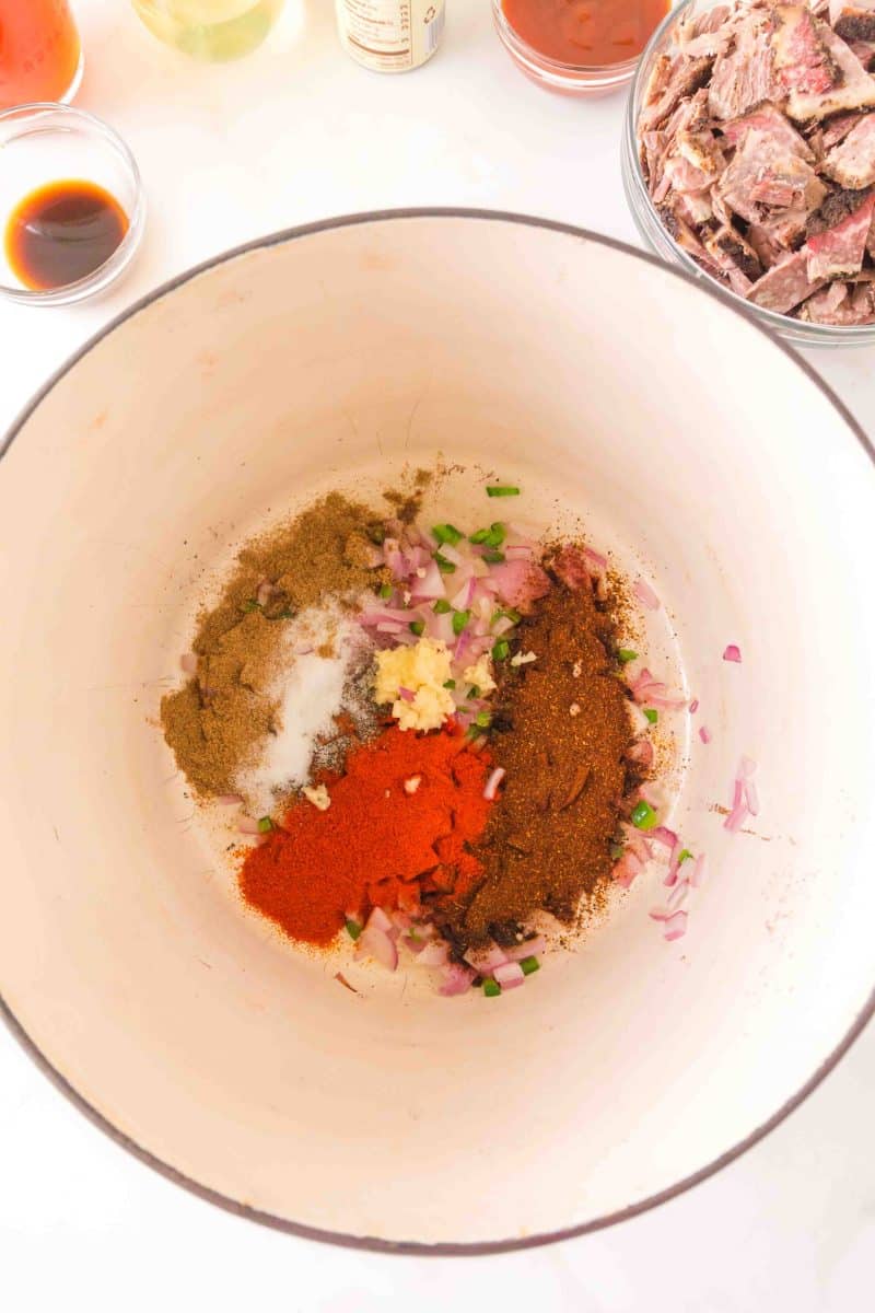 Overhead view of a Dutch oven filled with sauteed onion and jalapeno topped with spices. Hostess At Heart