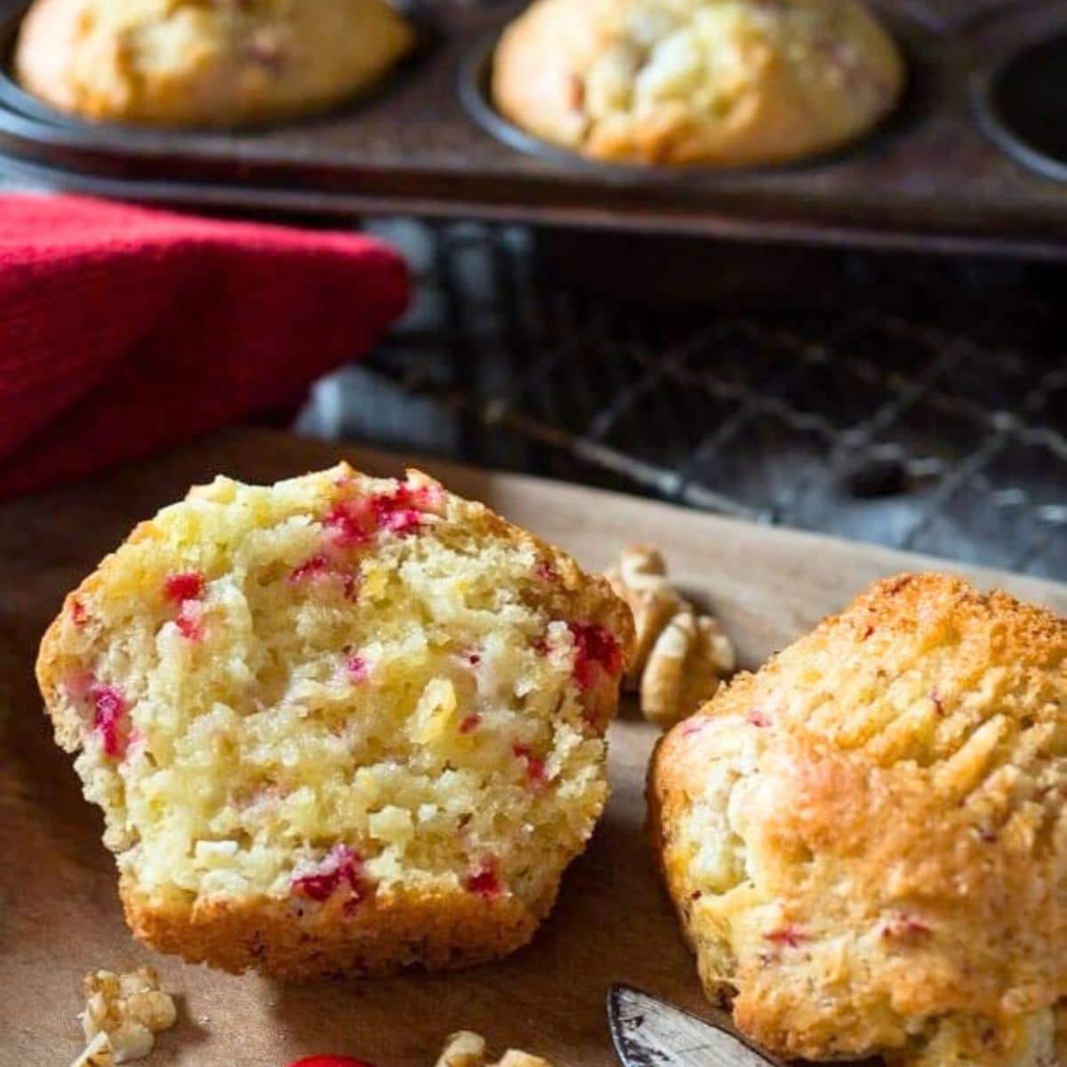A golden brown moist muffin split in half showing pieces of chopped cranberries and walnuts and a golden brown expterior. Hostess At Heart