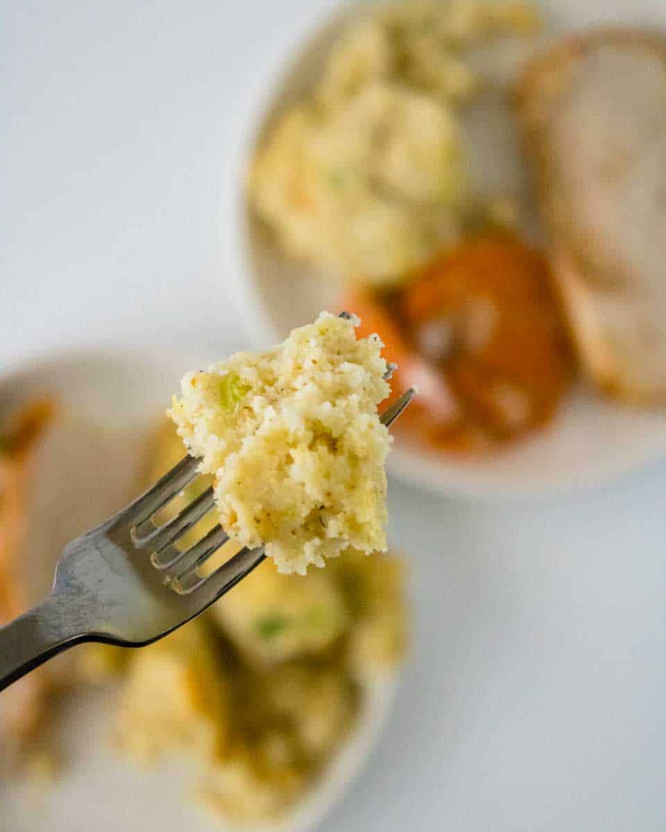 A fork filled with cornbread stuffing showing a moist fluffy bite. Hostess At Heart