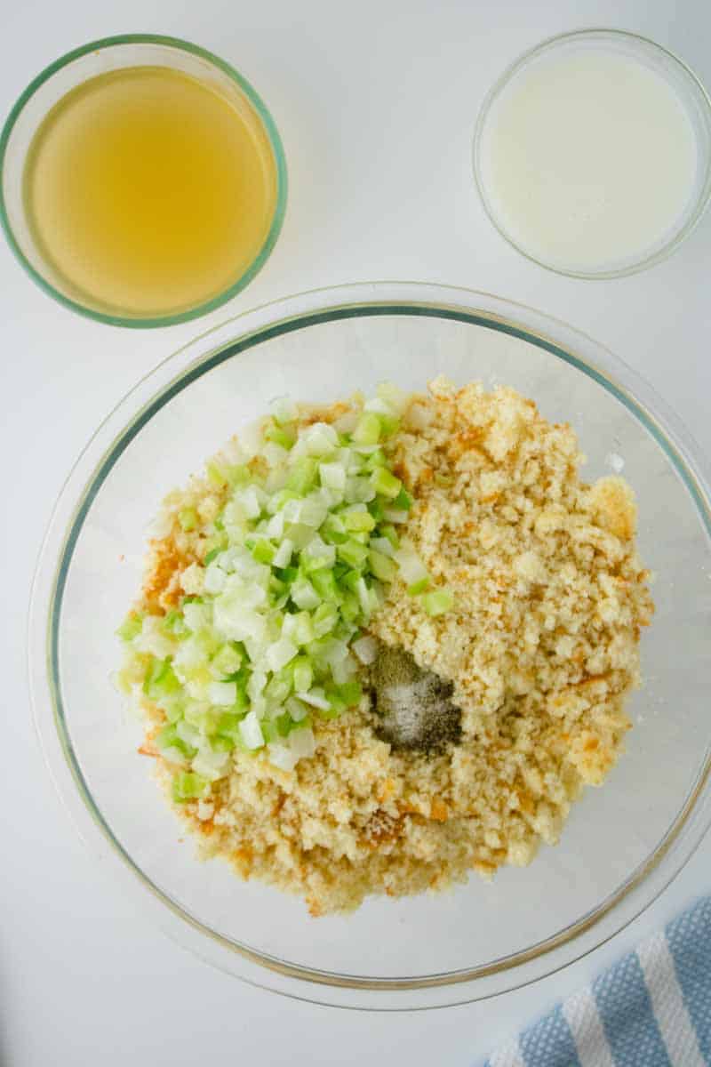 A large mixing bowl filled with crumbled cornbread, celery, onion, and spices to make a cornbread dressing recipe. Hostess At Heart