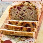 Front view of a sliced loaf of bread loaded with cranberries and walnuts sitting on a cutting board. Hostess At Heart