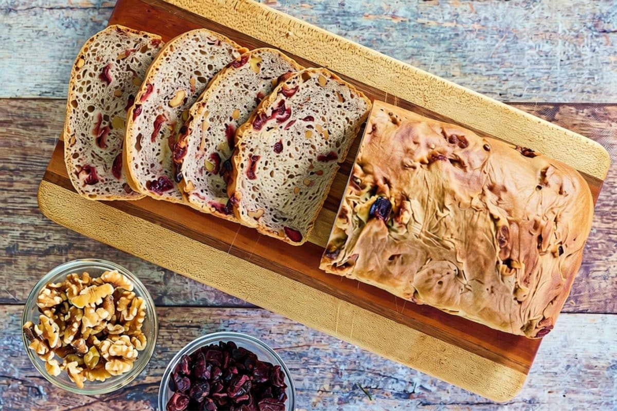 Top down view of a sliced loaf of cranberry walnut bread sitting on a cutting board. Hostess At Heart