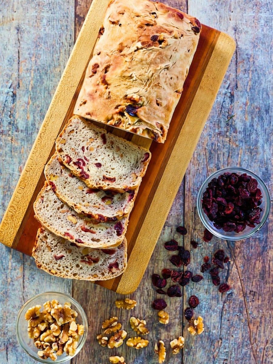 Top down view of a sliced loaf of cranberry walnut bread on a cutting board. Hostess At Heart