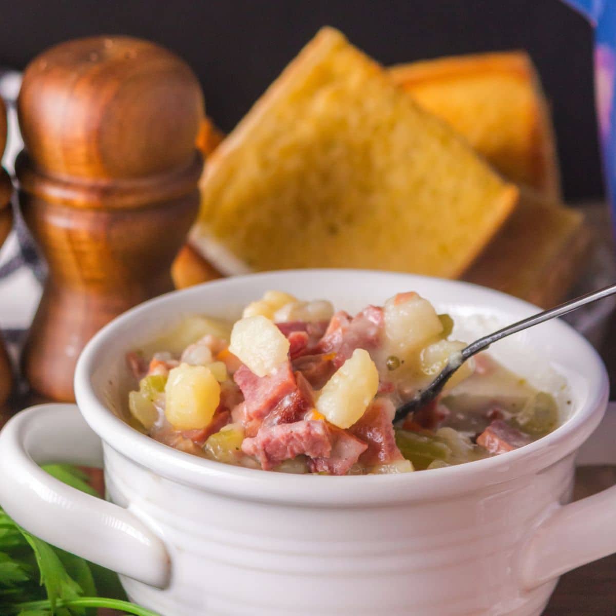 A spoon lifting a bite of creamy ham and potato soup with ham and vegetables. Hostess At Heart