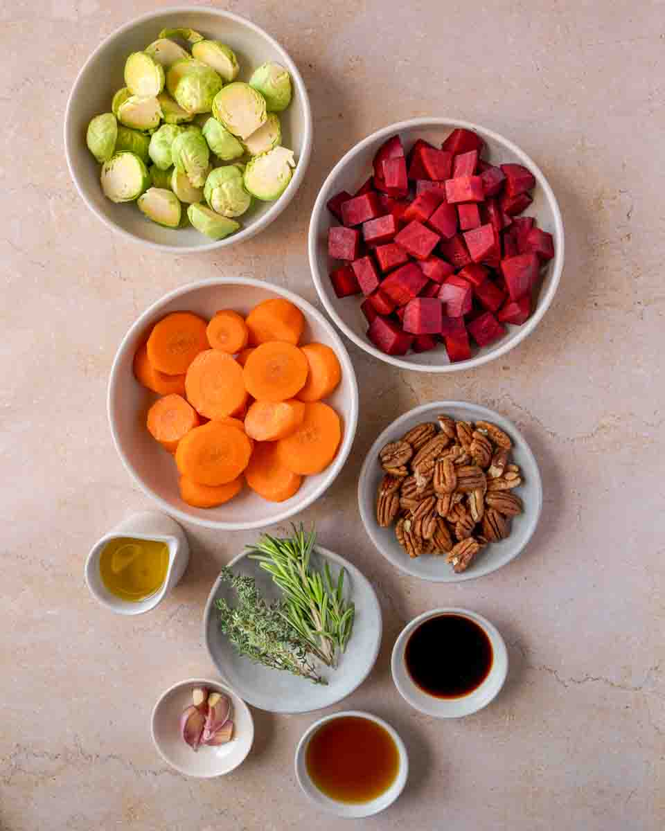 Holiday roasted vegetable recipe ingredients: sliced carrots, halved Brussels sprouts, olive oil, honey, balsamic vinegar, garlic cloves, diced beets, fresh thyme, and fresh rosemary. Hostess At Heart