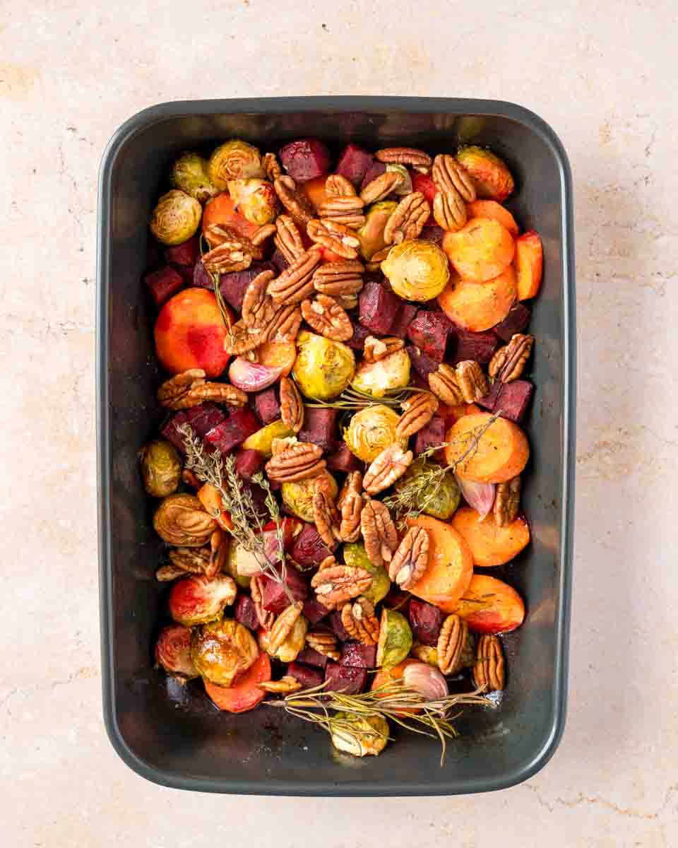 A baking dish hot from the oven filled with carrots, beets, Brussels sprout halves with herbs and pecans. Hostess At Heart