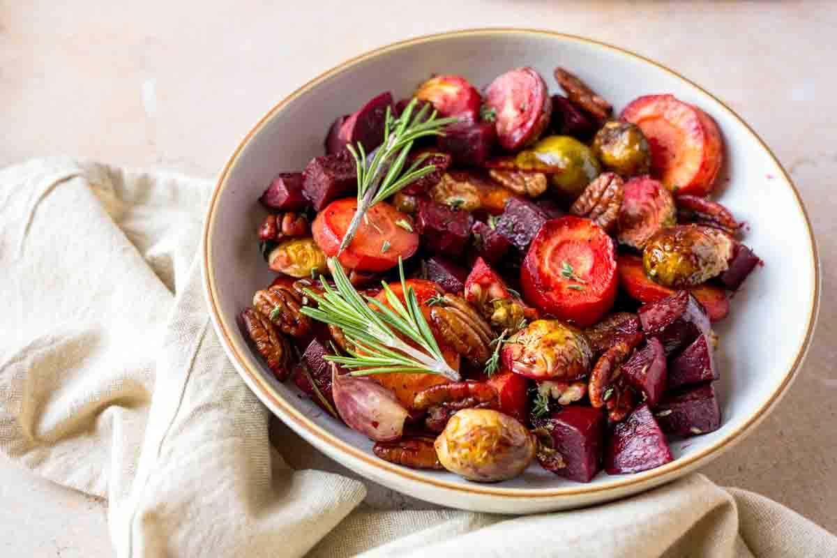 A serving bowl filled with Honey Roasted carrots, beets, and Brussels sprouts with pecans in a serving dish. Hostess At Heart