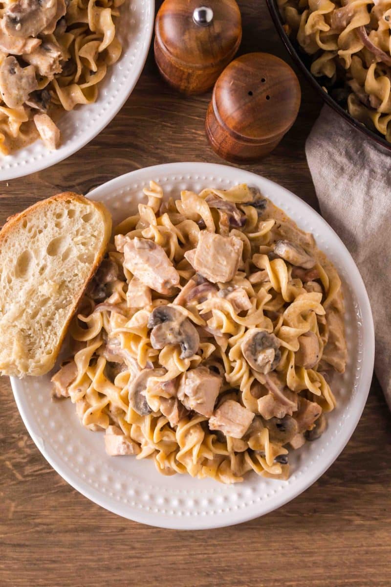A white dinner plate topped with a serving of turkey stroganoff with leftover turkey, mushrooms, and egg noodles. Hostess At Heart