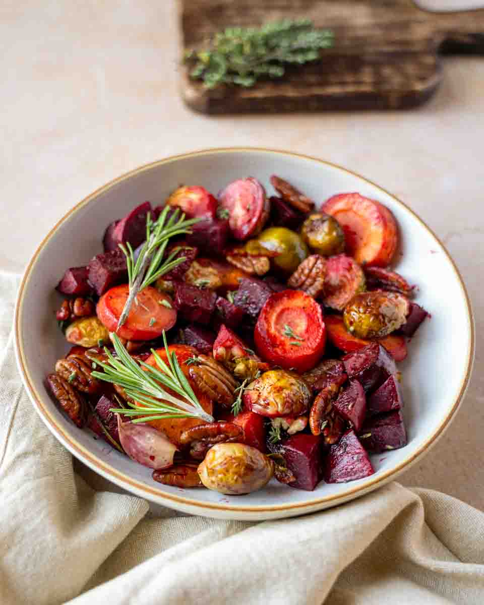 A holiday medley of roasted beets, Brussels sprouts, carrots in a balsamic sauce, topped with herbs and pecans in a serving bowl. Hostess At Heart